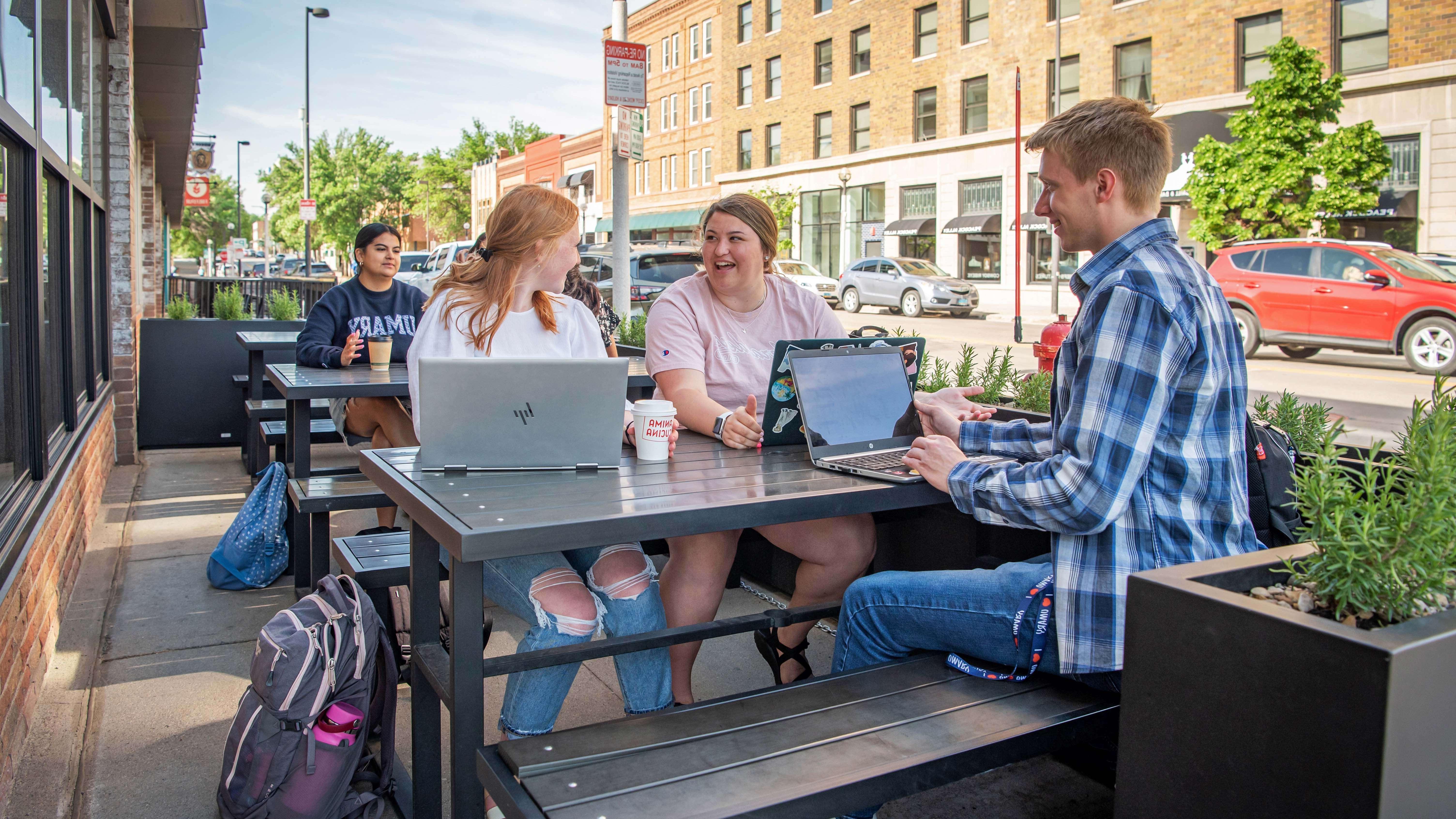 三个立博中文版的学生坐在俾斯麦市中心一家餐厅外的野餐桌旁